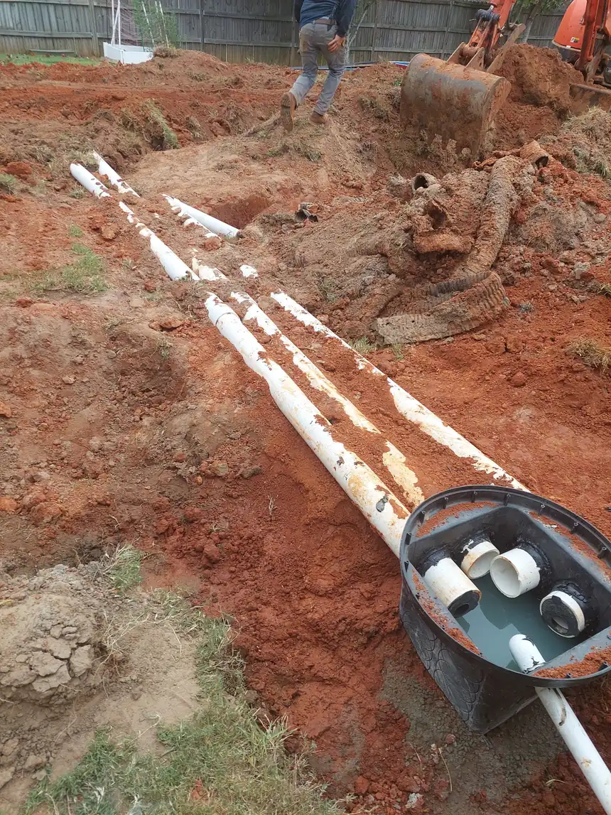 Open drainage trench in Georgia red clay with white PVC drain lines, a catch basin and a mini excavator on a Warner Robins job