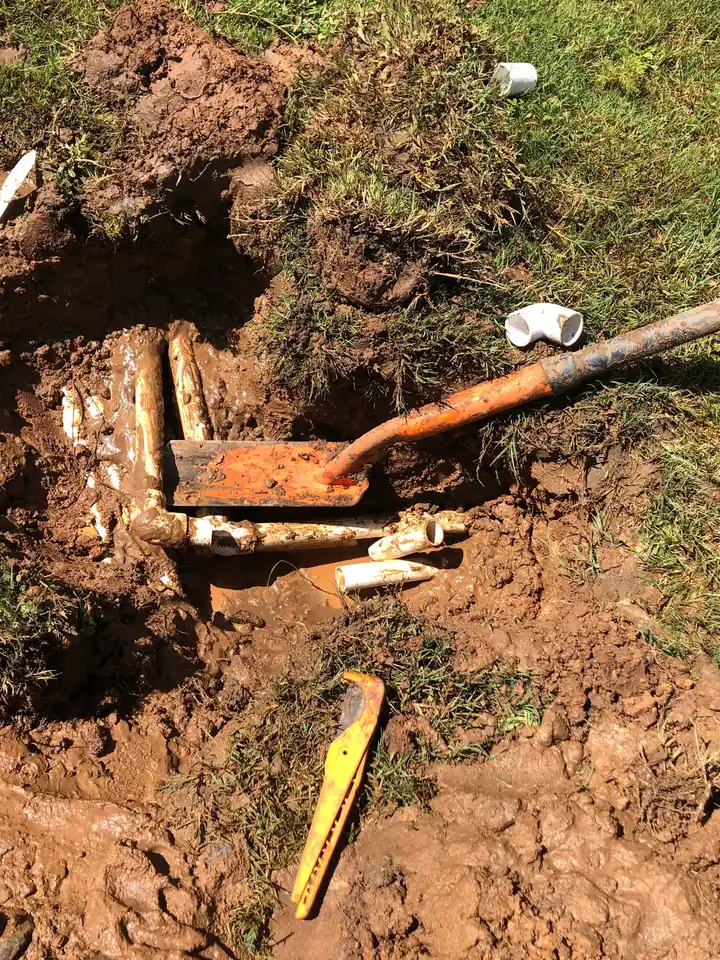 Excavated hole in a lawn showing a cut PVC sprinkler line and elbow fittings during an irrigation repair